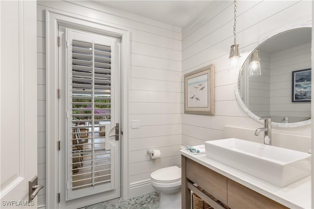 bathroom with vanity, toilet, and wood walls