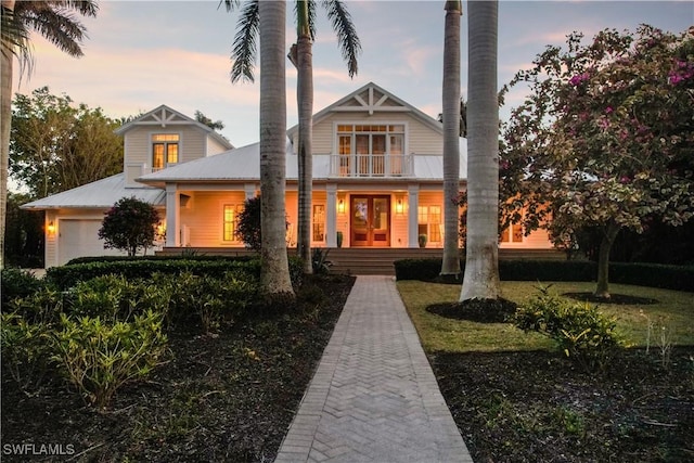 back house at dusk featuring a balcony and a garage