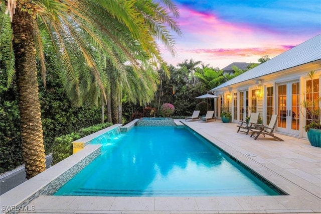 pool at dusk with pool water feature, a patio, and french doors