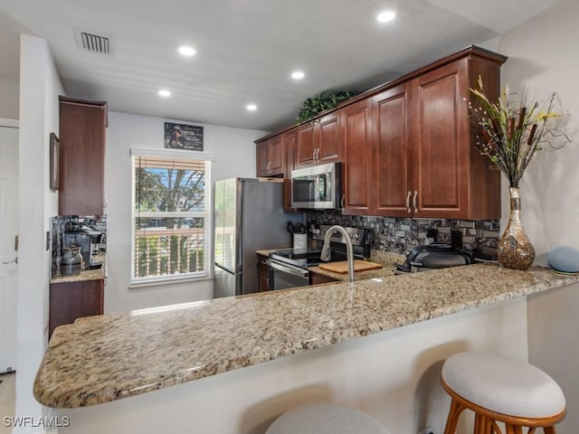 kitchen with kitchen peninsula, appliances with stainless steel finishes, backsplash, and a kitchen breakfast bar