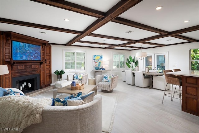 living room featuring light wood finished floors, visible vents, beamed ceiling, and a large fireplace