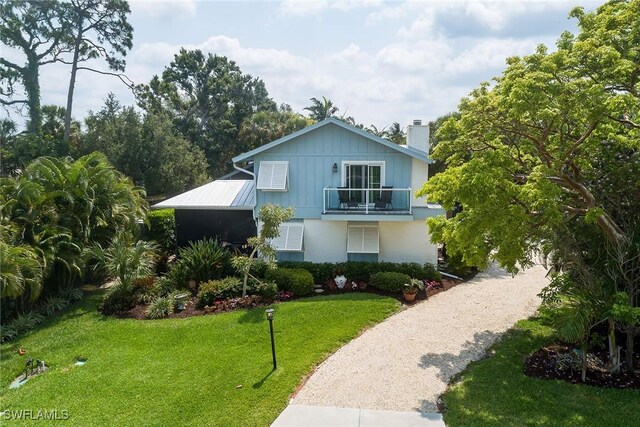 view of front of home with a front yard, a balcony, driveway, a chimney, and metal roof