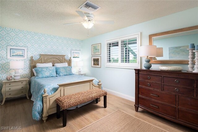 bedroom featuring wallpapered walls, visible vents, baseboards, and a textured ceiling