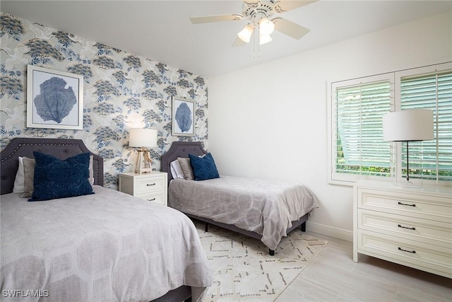 bedroom featuring wallpapered walls, an accent wall, baseboards, wood finished floors, and a ceiling fan