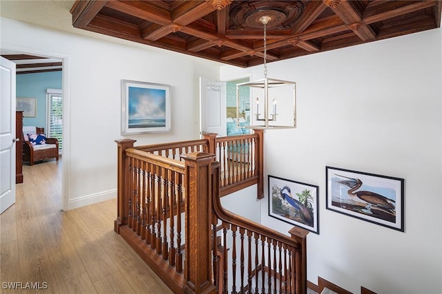 hallway with baseboards, coffered ceiling, light wood finished floors, beamed ceiling, and an upstairs landing