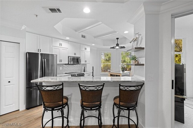 kitchen featuring backsplash, kitchen peninsula, light stone counters, white cabinetry, and stainless steel appliances