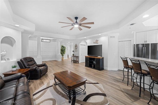 living room featuring decorative columns, a raised ceiling, ceiling fan, and light hardwood / wood-style floors