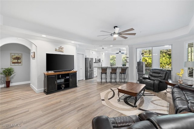 living room with ceiling fan, a raised ceiling, light wood-type flooring, and crown molding