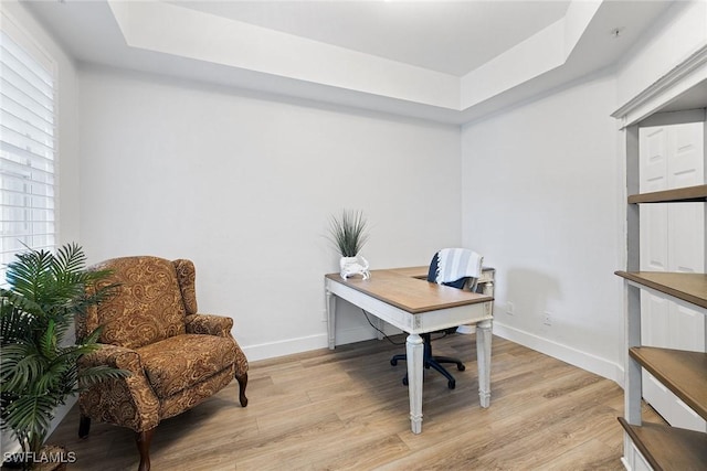 home office with light wood-type flooring and a tray ceiling