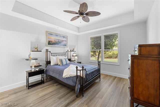 bedroom featuring light wood-type flooring, a raised ceiling, and ceiling fan