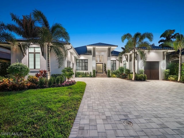 view of front facade featuring a garage, metal roof, decorative driveway, and stucco siding