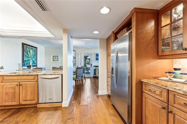 kitchen with sink, stainless steel appliances, light stone counters, backsplash, and light hardwood / wood-style floors