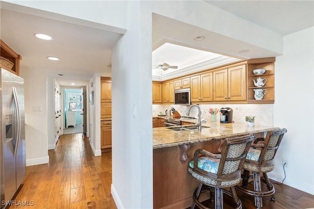 kitchen with kitchen peninsula, appliances with stainless steel finishes, light stone counters, and sink