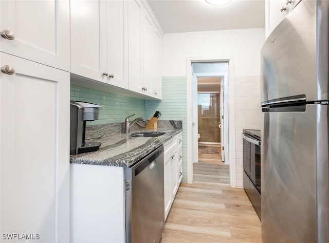 kitchen featuring white cabinetry, sink, stainless steel appliances, dark stone countertops, and light hardwood / wood-style floors