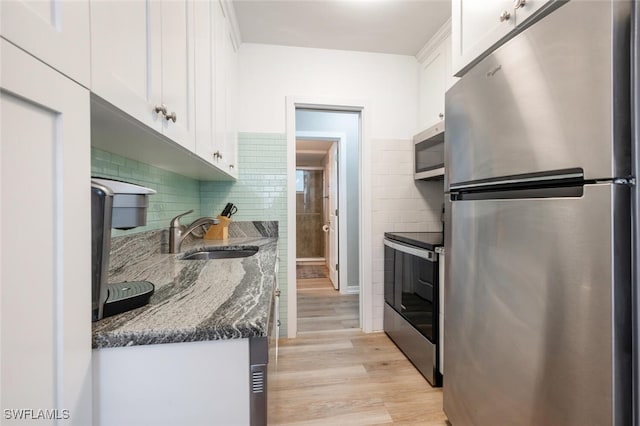 kitchen featuring dark stone counters, sink, light hardwood / wood-style flooring, white cabinetry, and stainless steel appliances