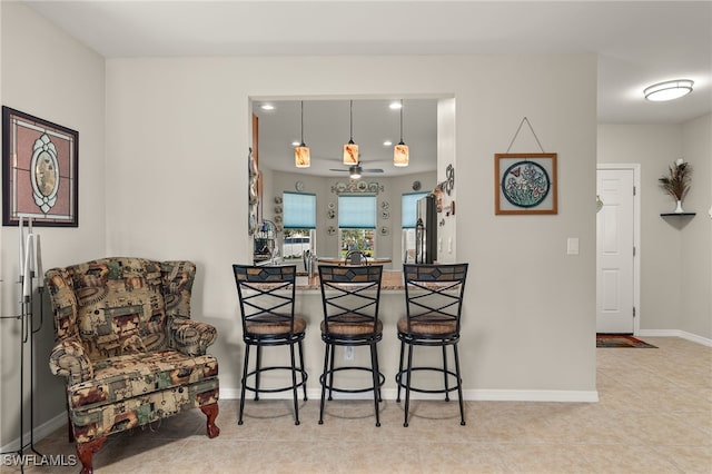 kitchen featuring hanging light fixtures, ceiling fan, light tile patterned floors, a breakfast bar area, and stainless steel refrigerator