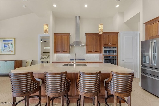 kitchen with pendant lighting, wall chimney exhaust hood, a kitchen bar, stainless steel appliances, and a kitchen island with sink