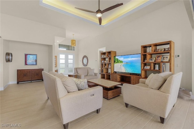 living room with ceiling fan, a tray ceiling, light hardwood / wood-style flooring, and french doors