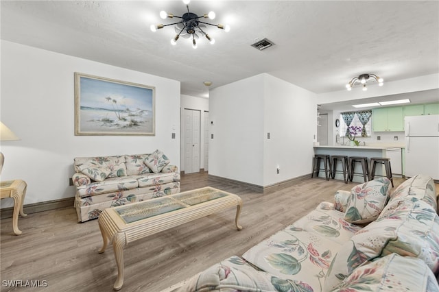 living room featuring a textured ceiling, a notable chandelier, and light wood-type flooring