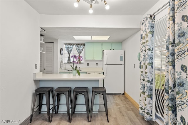 kitchen featuring a breakfast bar, green cabinets, light hardwood / wood-style flooring, white fridge, and kitchen peninsula