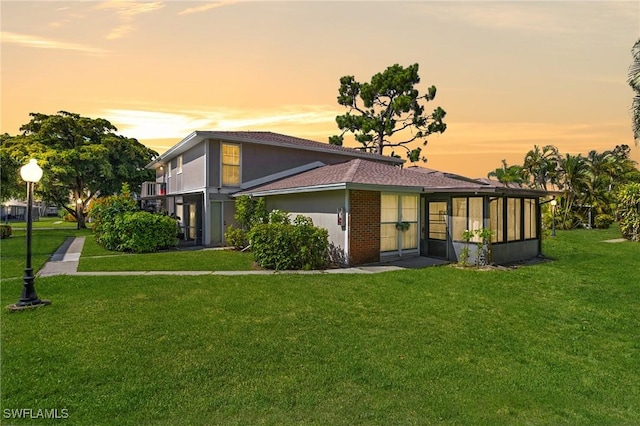 back house at dusk featuring a lawn and a sunroom