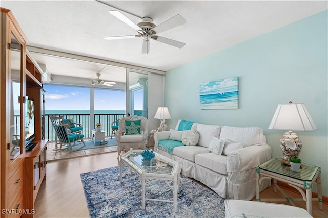 living room featuring ceiling fan, expansive windows, a water view, and wood-type flooring