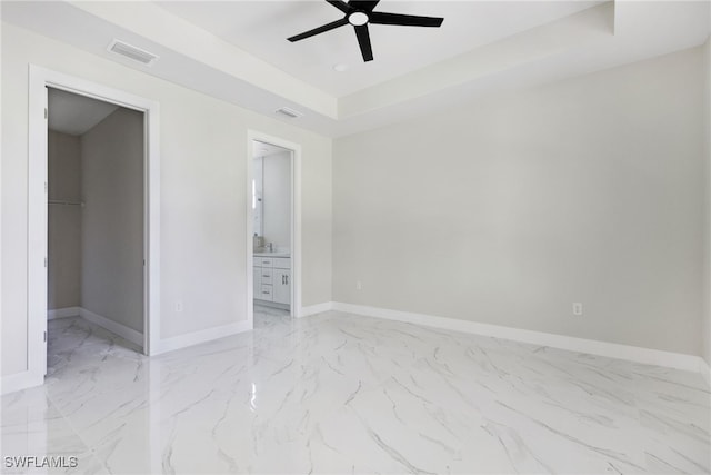 unfurnished bedroom featuring a closet, a spacious closet, ceiling fan, and a tray ceiling