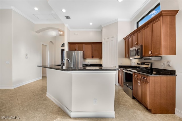 kitchen featuring dark stone counters, stainless steel appliances, crown molding, and a center island with sink