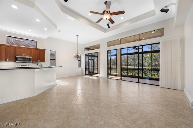 unfurnished living room with a high ceiling, ceiling fan with notable chandelier, and a raised ceiling