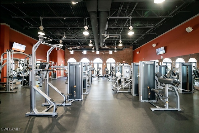 gym featuring a high ceiling, track lighting, and brick wall