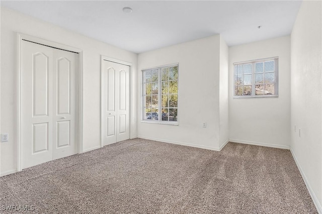 unfurnished bedroom with carpet, multiple windows, and multiple closets