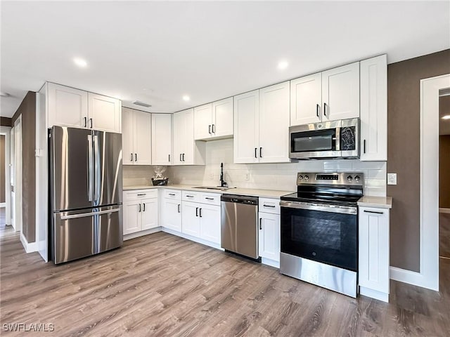 kitchen with white cabinetry, sink, stainless steel appliances, light hardwood / wood-style floors, and decorative backsplash