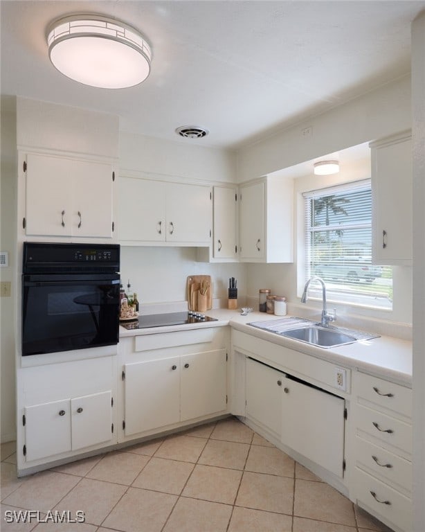 kitchen with white cabinets, sink, light tile patterned floors, black oven, and cooktop