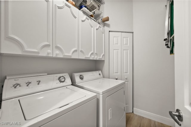 washroom with light wood-type flooring, washer and dryer, and cabinets