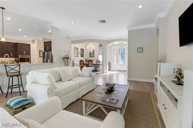 living room featuring light hardwood / wood-style floors, an inviting chandelier, ornamental molding, and sink