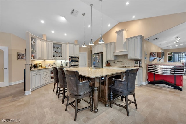 kitchen with hanging light fixtures, tasteful backsplash, a kitchen breakfast bar, premium range hood, and an island with sink