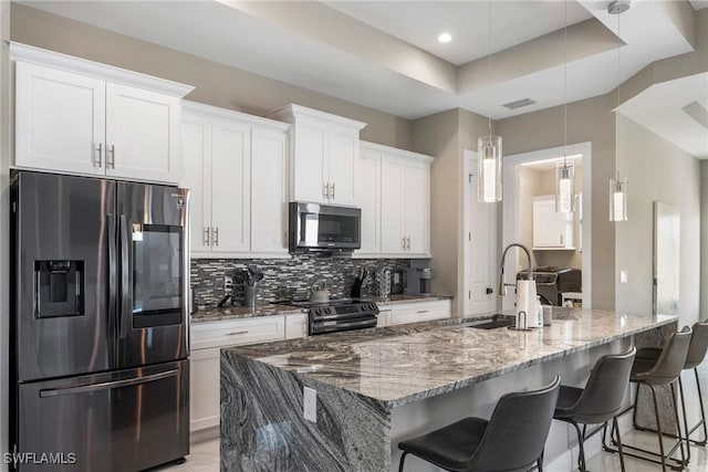 kitchen featuring light stone countertops, appliances with stainless steel finishes, a raised ceiling, pendant lighting, and white cabinetry