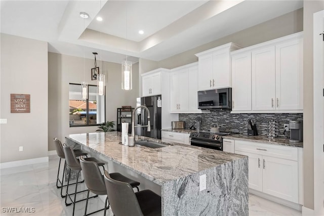 kitchen featuring stainless steel fridge, a kitchen island with sink, range with electric cooktop, a tray ceiling, and white cabinets