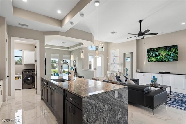 kitchen featuring stainless steel dishwasher, dark stone counters, a raised ceiling, sink, and washer / dryer