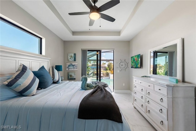 bedroom with ceiling fan, access to exterior, and a tray ceiling