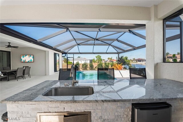 view of patio with glass enclosure, ceiling fan, and a wet bar