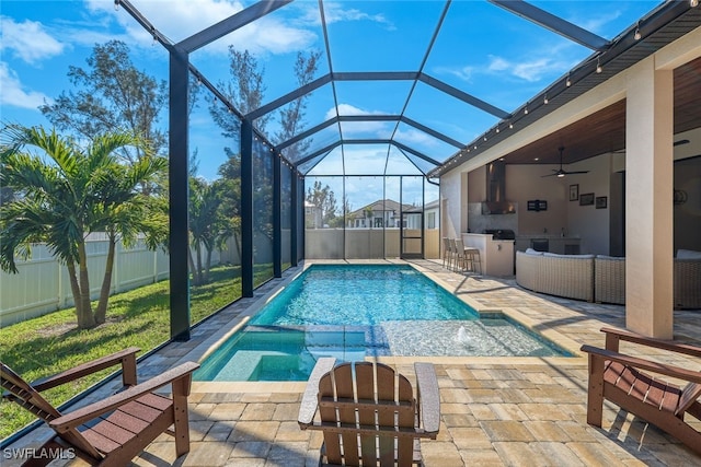 view of swimming pool featuring glass enclosure, a patio, an outdoor kitchen, and ceiling fan