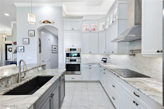 kitchen with stainless steel double oven, wall chimney range hood, decorative light fixtures, white cabinets, and sink