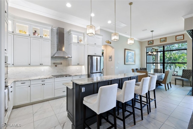 kitchen with wall chimney exhaust hood, a kitchen island, decorative light fixtures, white cabinetry, and stainless steel refrigerator