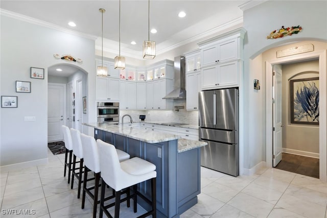 kitchen with appliances with stainless steel finishes, wall chimney exhaust hood, white cabinets, light stone counters, and decorative backsplash