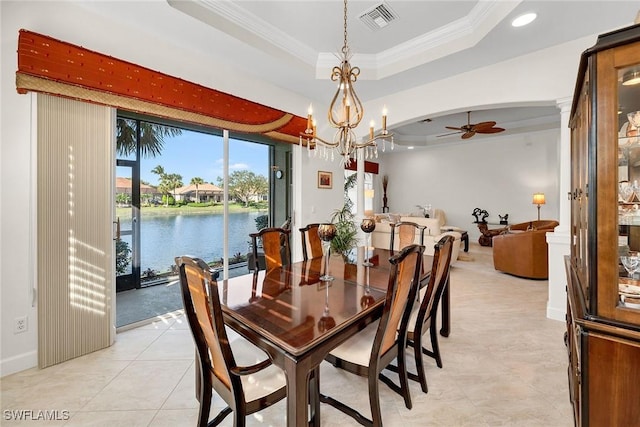 tiled dining room featuring a raised ceiling, a water view, ceiling fan with notable chandelier, and ornamental molding