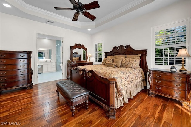 bedroom featuring ornamental molding, ensuite bathroom, dark hardwood / wood-style flooring, and a tray ceiling