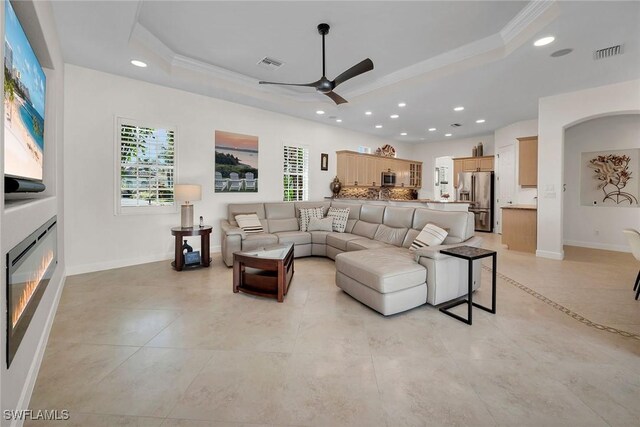 tiled living room featuring ceiling fan, ornamental molding, and a tray ceiling