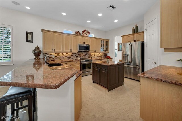 kitchen featuring sink, a center island, kitchen peninsula, a kitchen bar, and appliances with stainless steel finishes