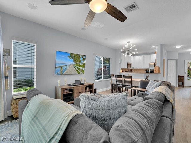 living room with ceiling fan with notable chandelier, light hardwood / wood-style flooring, and a healthy amount of sunlight